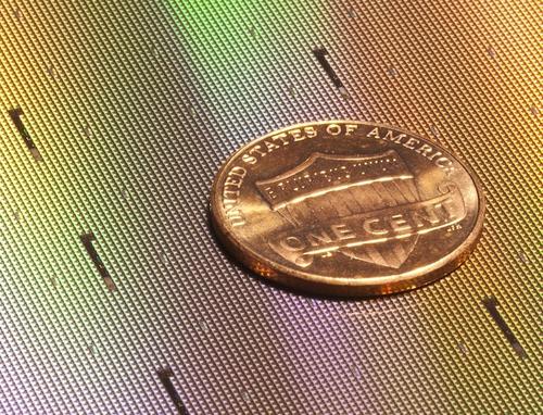 RFID chips, such as Impinj's Monza 5 devices, are dwarfed by a penny. Each tiny black square on the wafer in the background is one RFID chip.