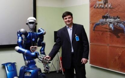 Associate Professor Vladimir Mulukha, PhD, Telematics Department of St. Petersburg Polytechnic University, shakes hands with the mobile humanoid 'Justin,' one type of robot utilized in Ford's space robots research project to advance connected-vehicle communications. (Photo: Ford Motor Co.)