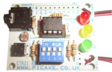 The AXE092 PICAXE Kit. The big black thing at the upper left is the programming socket. The small black thing at the lower left is a push switch. The DIP switch is for disconnecting outputs to use them for other things. The upper wires on the right-hand side go to the battery; wires on the lower right-hand side go to a piezo sounder.