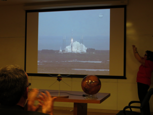 Fran Bagenal raising her hands in trump as the audience in the LASP auditorium watched the live broadcast of the MAVEN launch. A model of the satellite rests on the table next to the globe of Mars. (Source: Eric Bogatin)