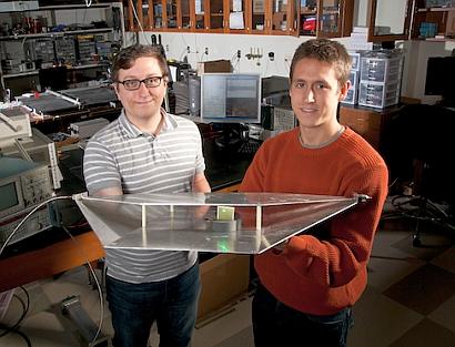 Duke engineering students Alexander Katko (left) and Allen Hawkes show a waveguide containing a single power-harvesting metamaterial cell, which provides enough energy to power the attached green LED.