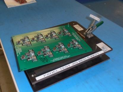 With this product, it is possible to test eight units simultaneously. Connections to each module are run across the breakout tabs and brought to a header on the panel that allows a connection to a test fixture. In this instance, the connector at the top is connected to a bed of nails. (Click here to see a larger image.)