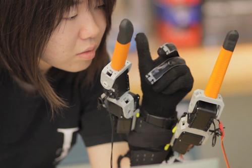 MIT doctoral candidate Faye Wu shows that by following the motions of the fingers the two robotic fingers adjacent to thumb and pinky can help users perform tasks with one hand that would ordinarily take two. (Source: MIT)